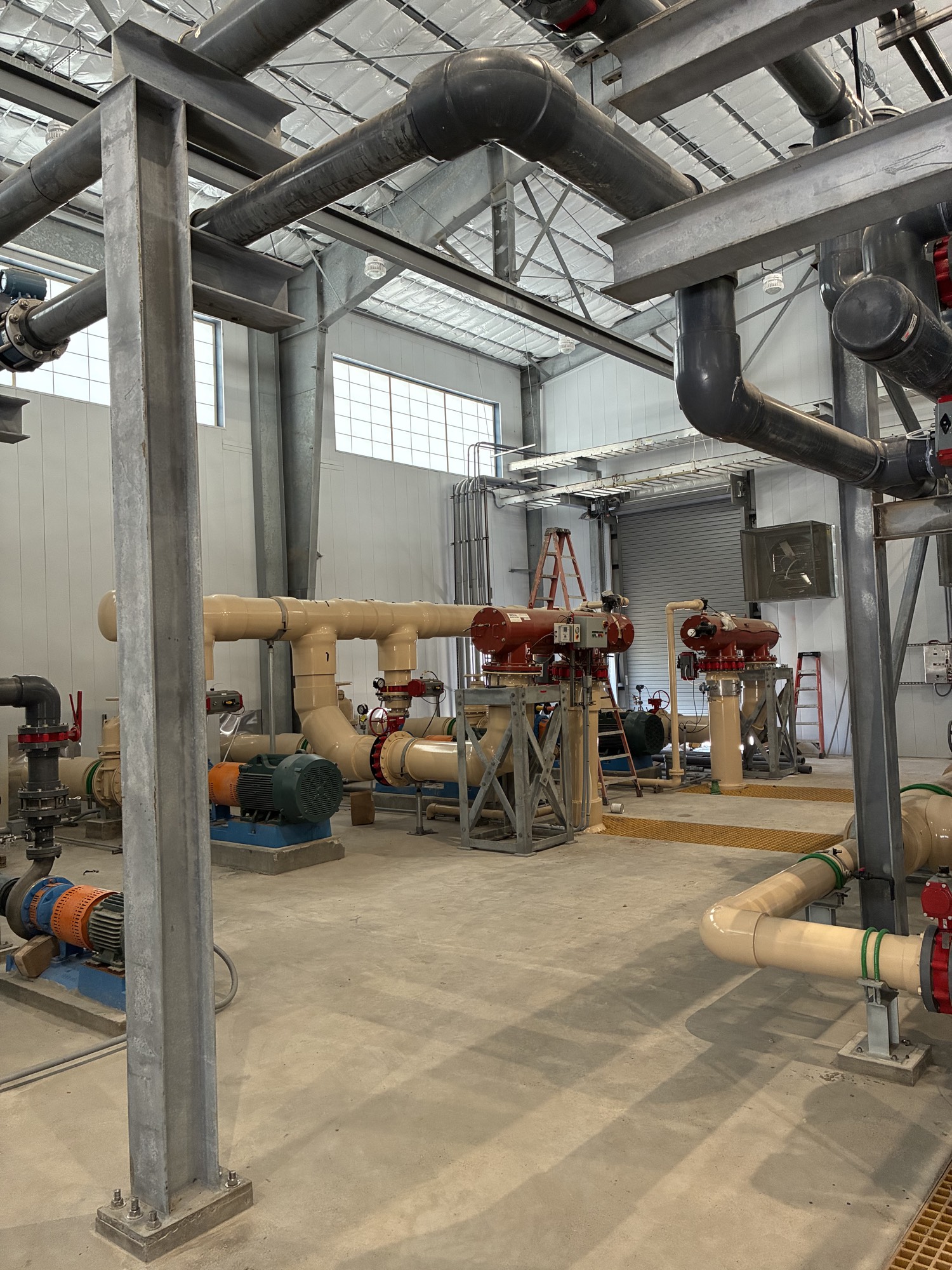 Wide angle view of industrial process piping and blue pipe racks inside a large metal building